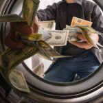 Photo of someone throwing bills of money into a washing machine, symbolizing money laundering.