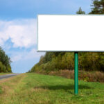 Big empty mockup Billboard along a highway with forest on background of blue sky with beautiful clouds on a bright sunny day.