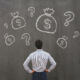 A person staring at a blackboard with images of money bags.