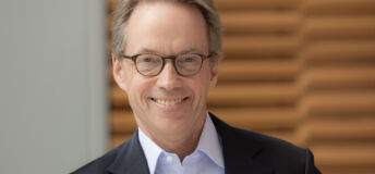 Headshot of Hamilton Lane wearing black blazer, light shirt and glasses against paneled background