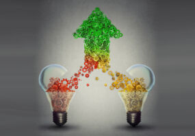 Teaming up concept: two open glass light bulbs releasing gears cogs coming together in the shape of upward arrow symbol