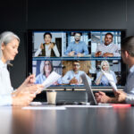 Global corporation online videoconference in meeting room with diverse people sitting in modern office and multicultural multiethnic colleagues on big screen monitor. Business technologies concept.