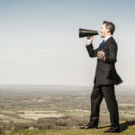 Picture of a businessman with loudhailer megaphone on hill.