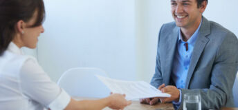 A smiling businessman receiving a resume from a young woman at a job interview