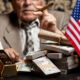 Image of a senior man behind stacks of dollar bills and constitution document.